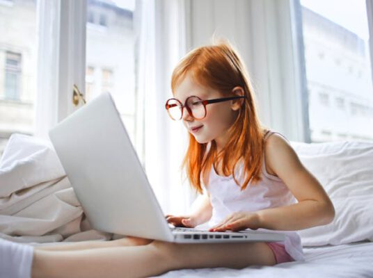 redhead kid with eye glasses working on a laptop